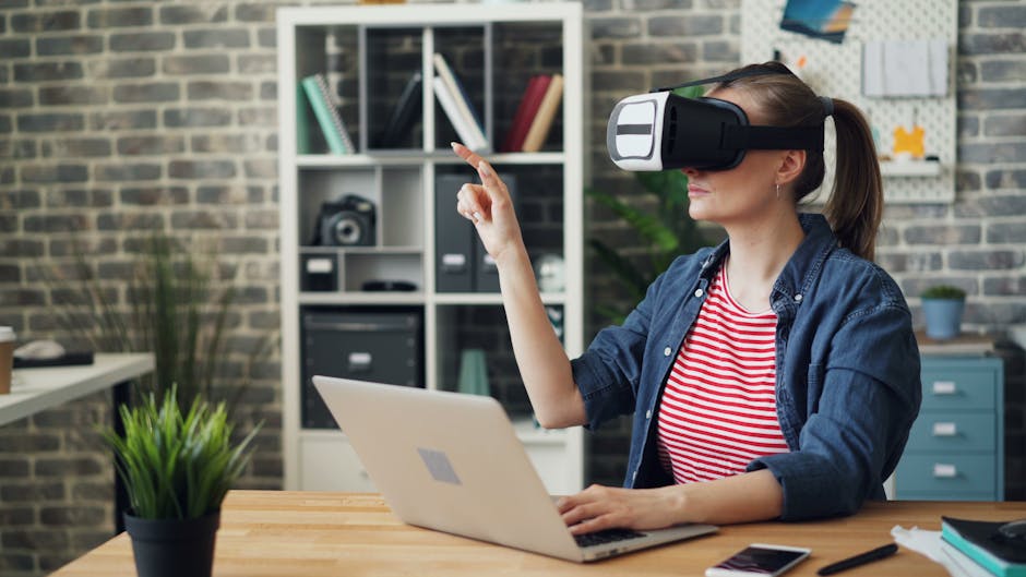 A woman using a VR headset while working on a laptop