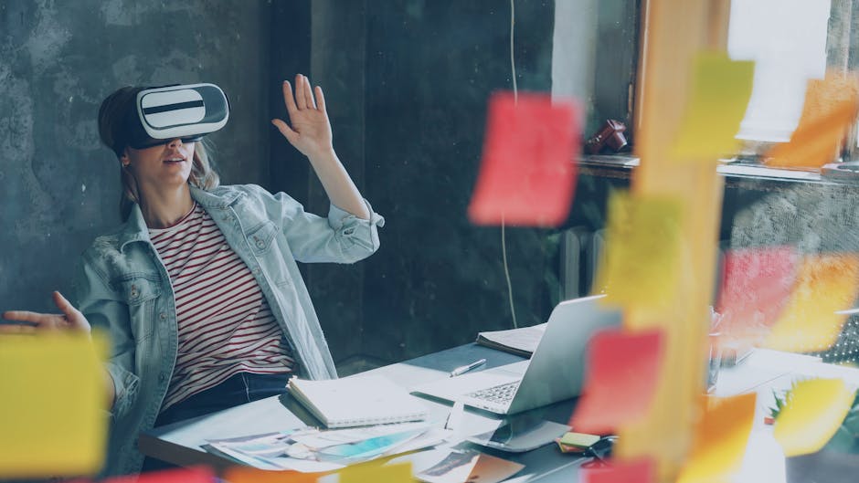 Woman using VR headset at desk, brainstorming with sticky notes and laptop